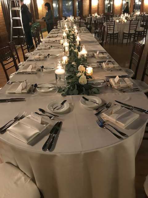 Long banquet table with candles, white roses runner, and place settings